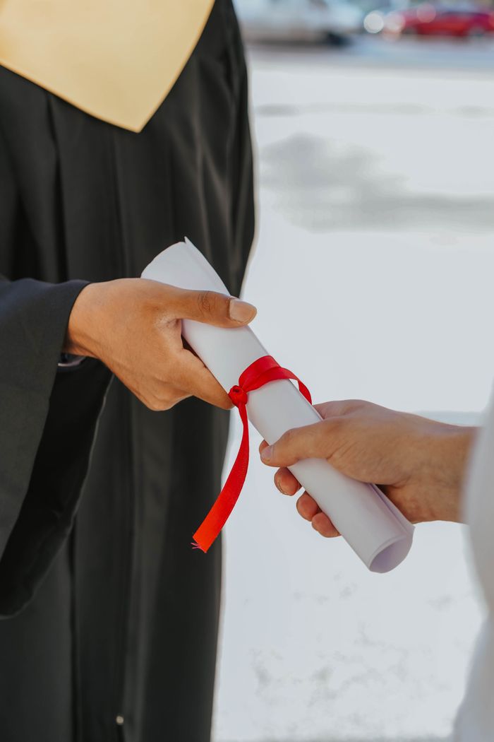 Mastering the First Impression: Your intriguing post title goes here Hands exchanging a graduation diploma wrapped with red ribbon, symbolizing achievement.